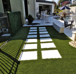 Close-up view of freshly installed synthetic turf, showcasing its lush green texture and precise installation around a residential patio area.