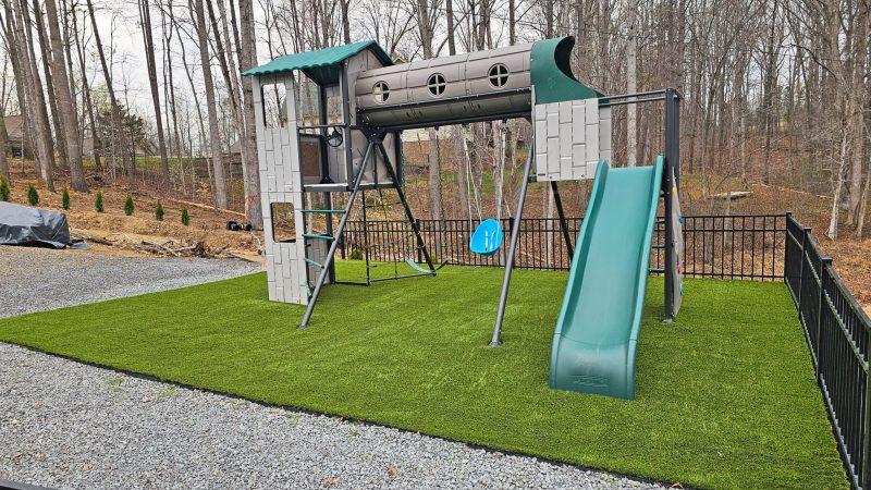 A newly installed Synthetic Turf Backyard Playground alongside a serene water body, blending natural beauty with playful design.