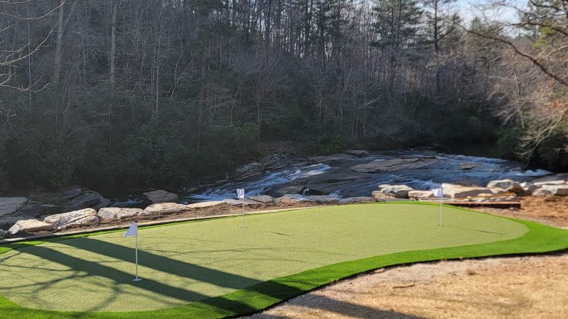Breathtaking artificial turf putting green by Synthetic Turf Concepts, nestled beside a serene water body and rugged landscape in Walhalla, SC